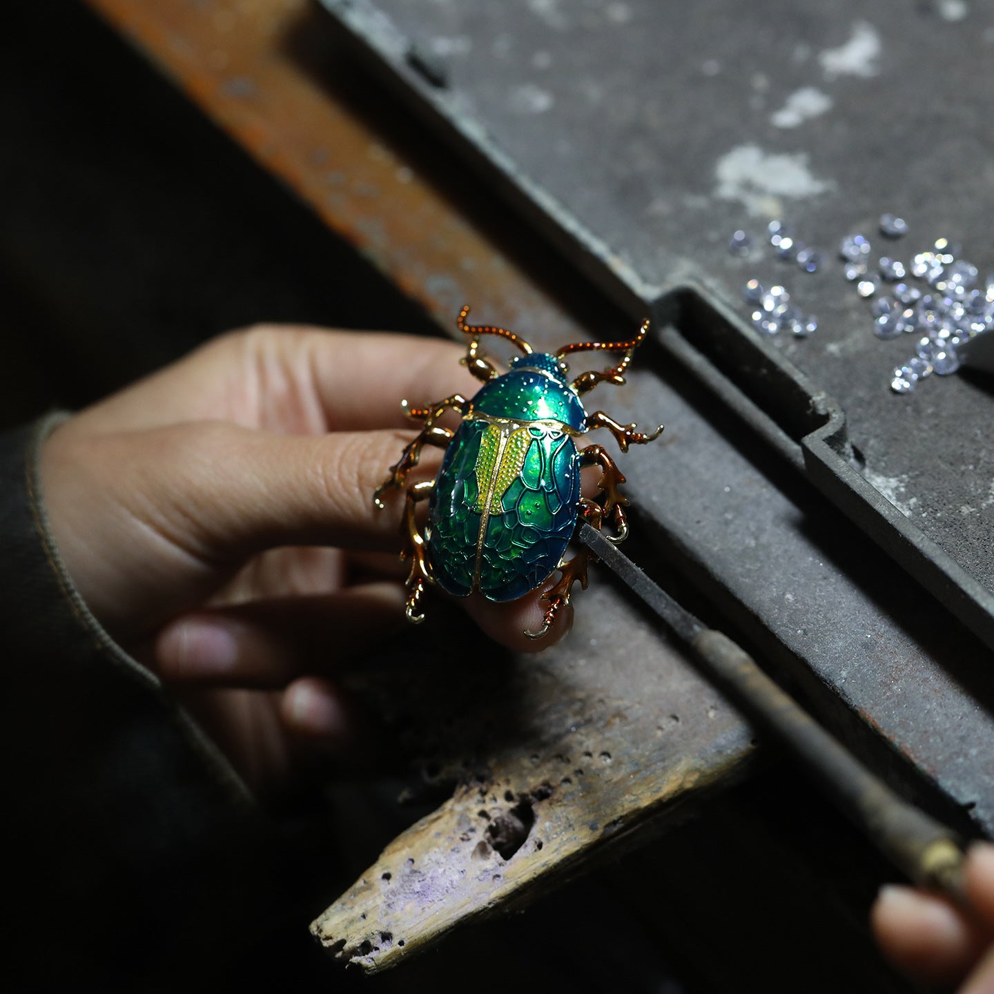 Hand holding a decorative beetle with gold and green colors on a dark surface.