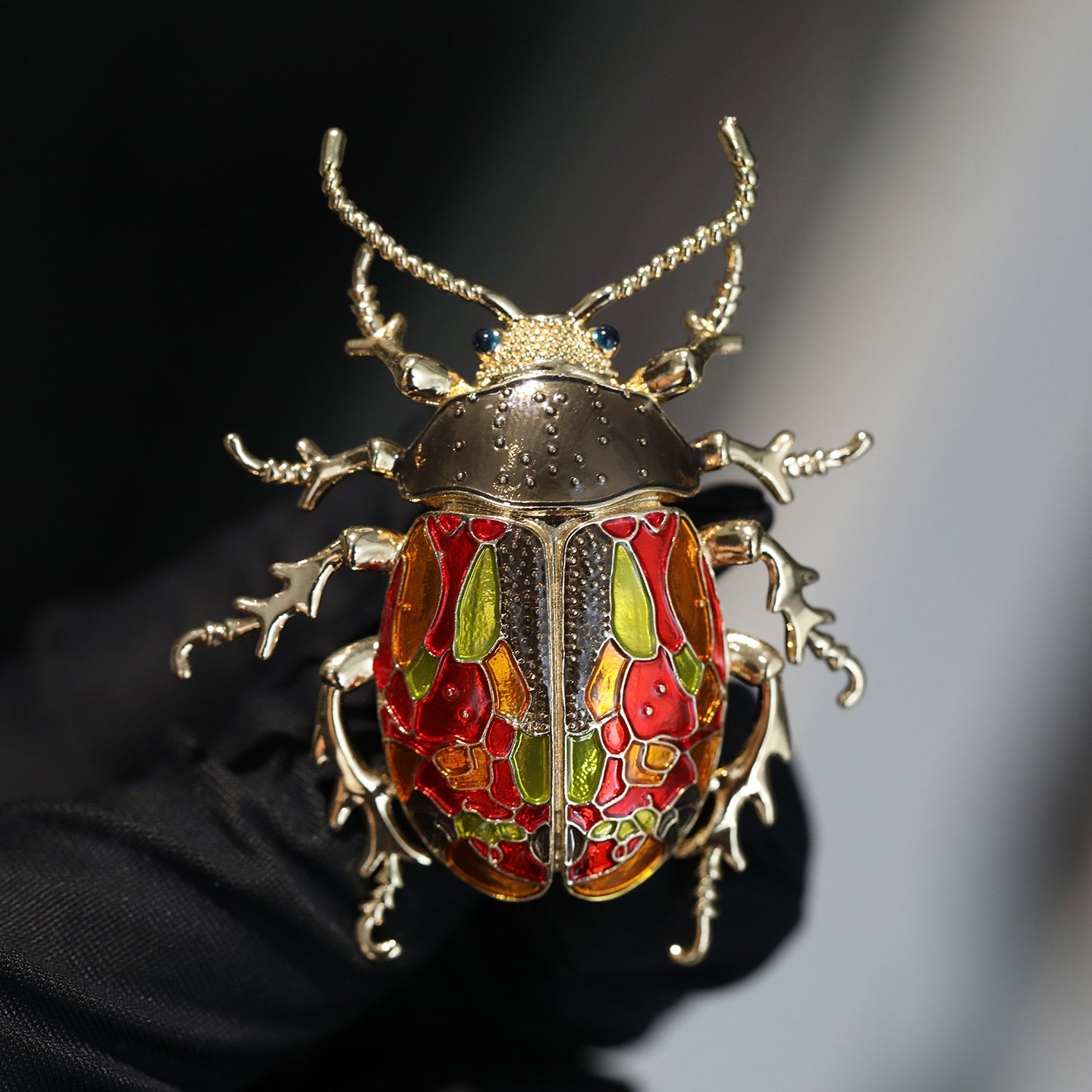 Decorative beetle brooch with gold, red, and green colors on a dark background