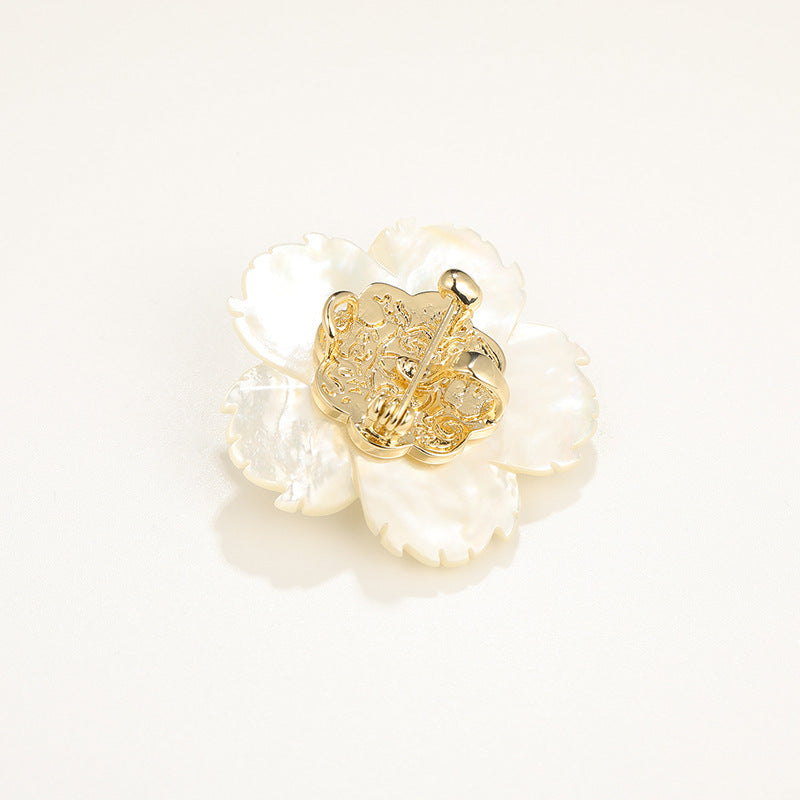 A gold flower-shaped brooch with iridescent white shell-like petals, photographed on a clean white background.