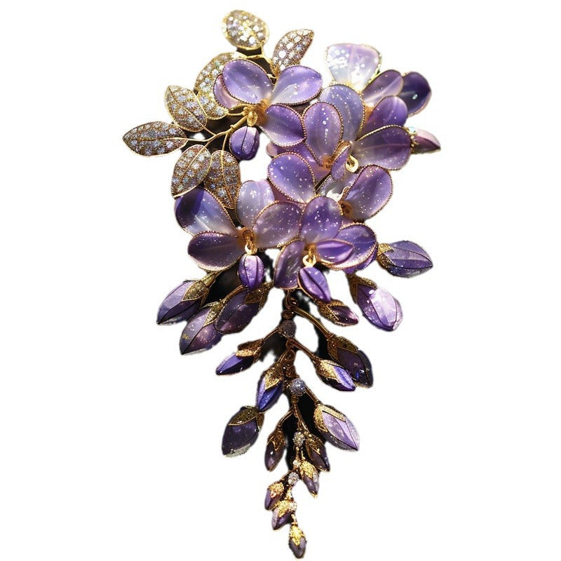A vintage-style brooch featuring purple wisteria flowers and leaves with gold-tone metal detailing and small clear rhinestone accents, shown against a plain white background.