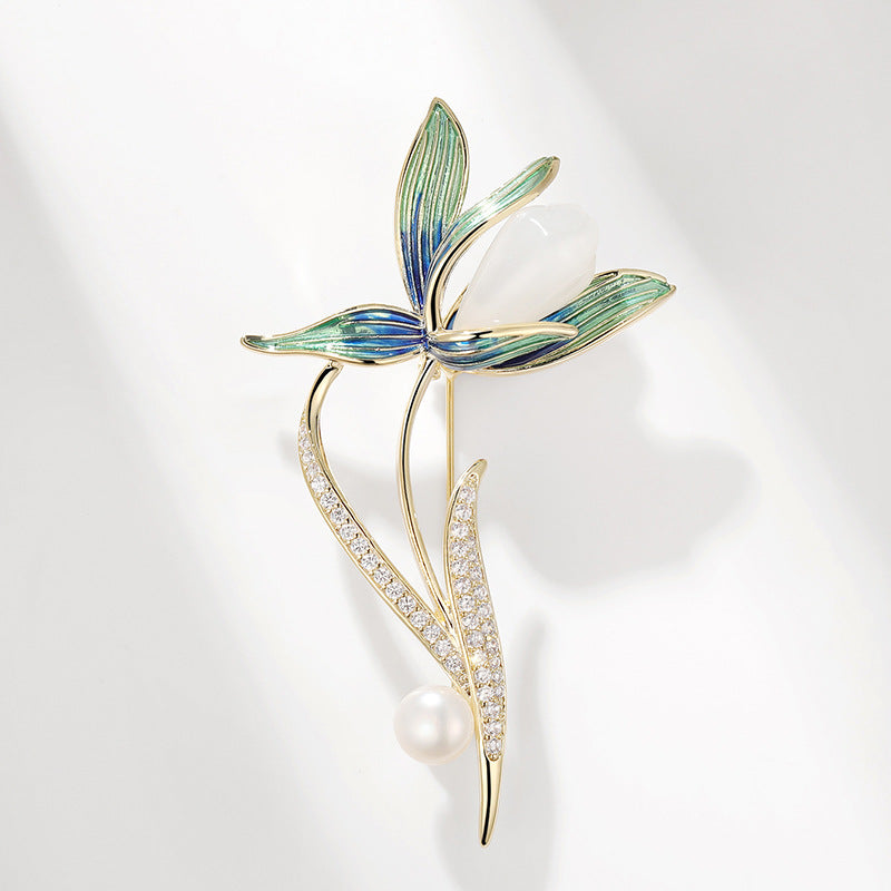 A gold-tone floral brooch featuring a butterfly with blue and green enamel wings, a pearl at the center, and a pearl and crystal-encrusted stem, set against a clean white background with soft shadows.