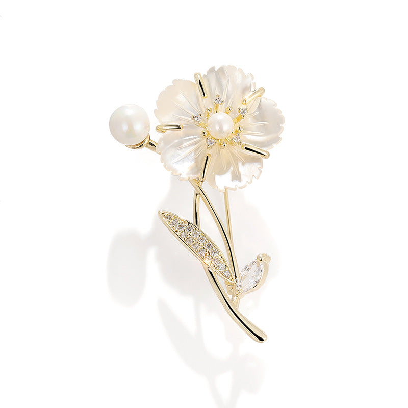 A gold flower brooch featuring a pearl flower with a gold center, a pearl bead on the stem, and a leaf adorned with small clear crystals, set against a clean white background.