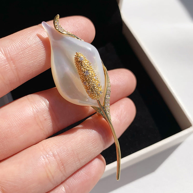 Gold leaf brooch held between fingers with a white box in the background