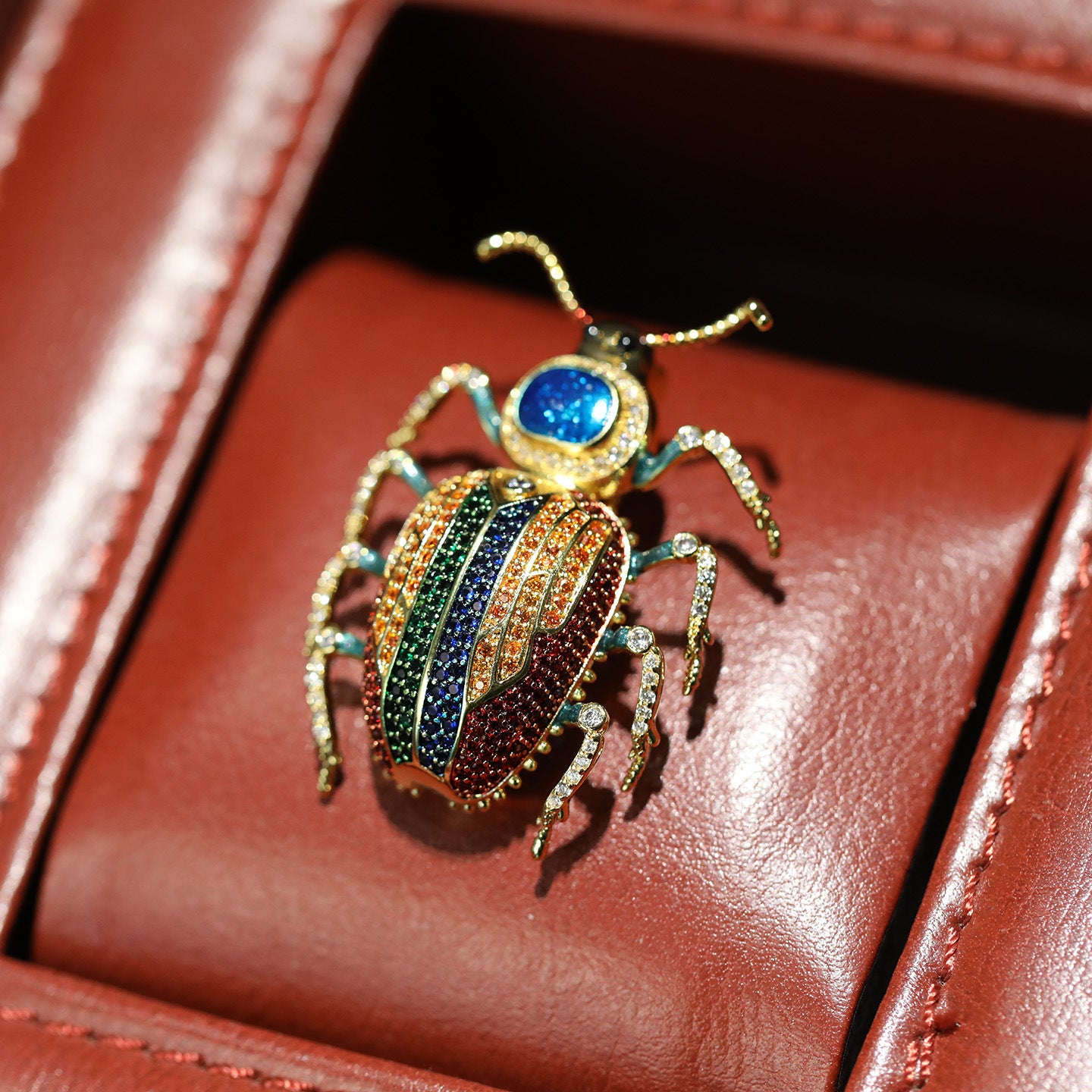 Colorful jeweled beetle brooch on a red leather surface