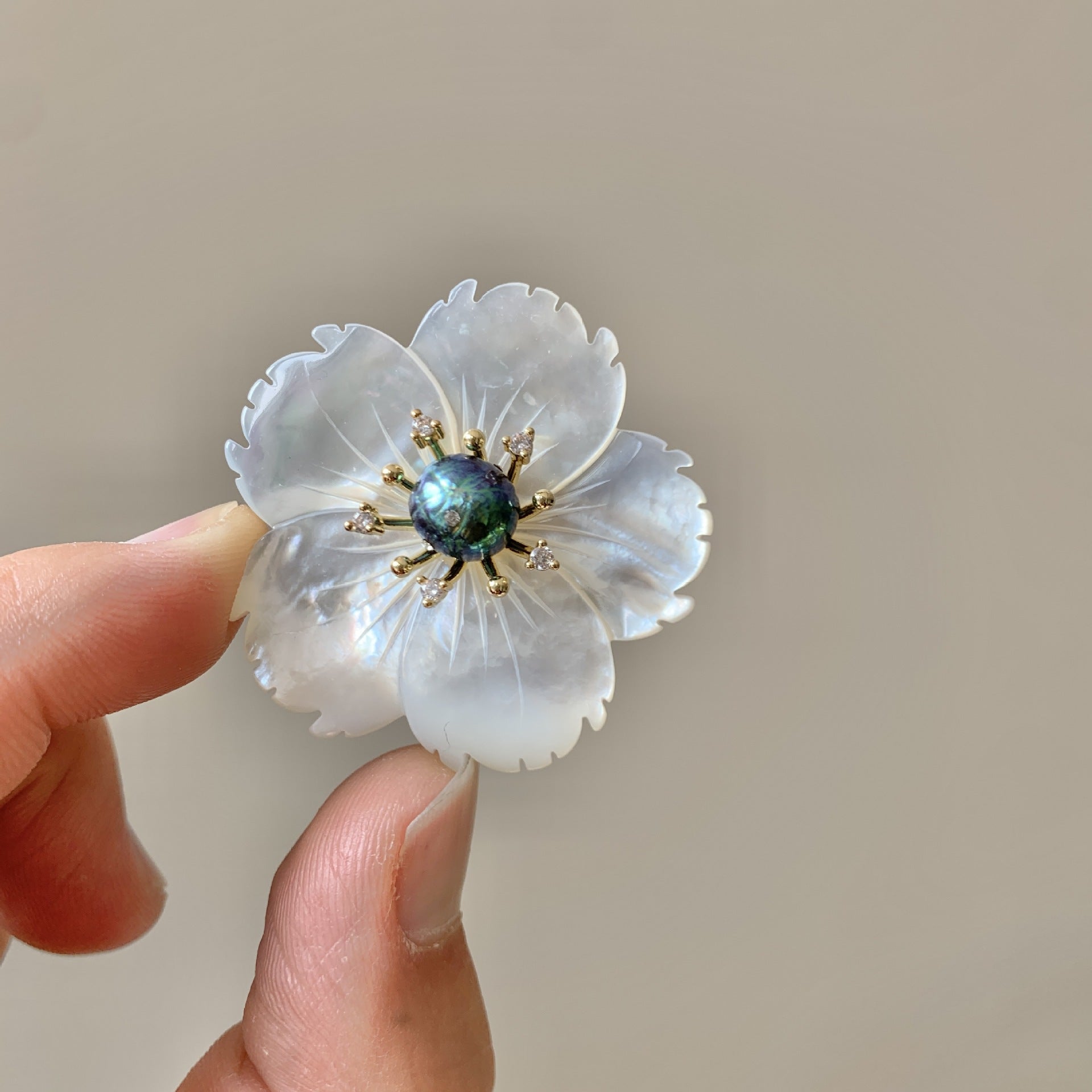 Floral brooch held between fingers against a neutral background