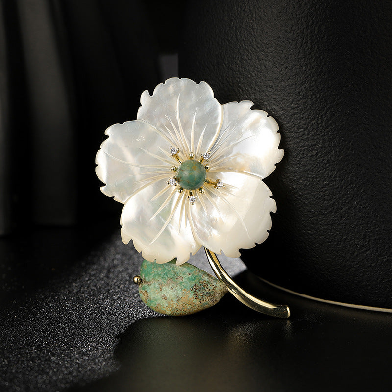 Floral brooch with white petals and green center on a dark background