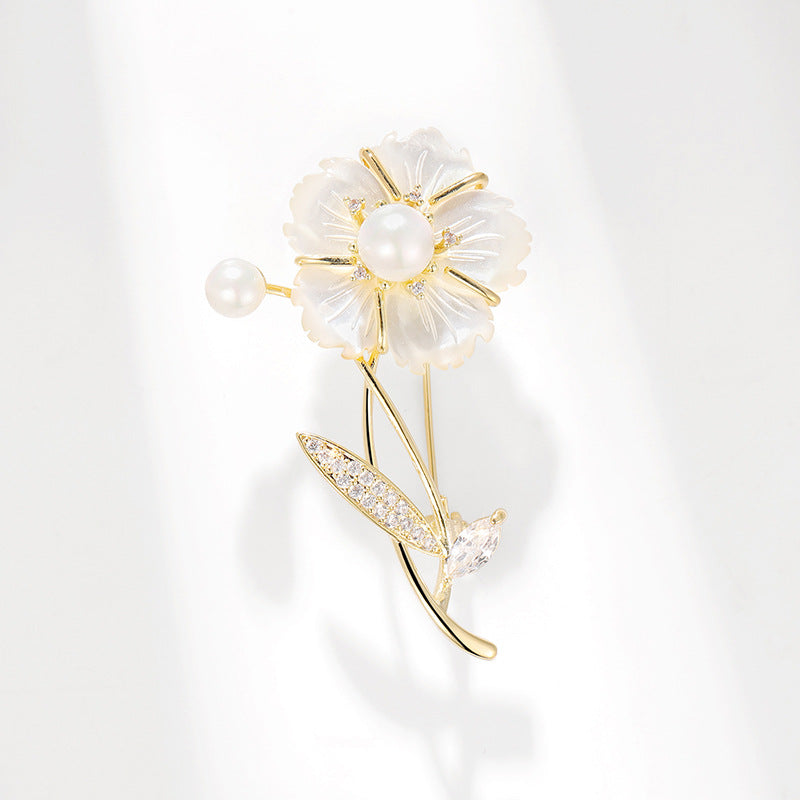 A gold-tone flower brooch featuring a pearl center and translucent white petal-like accents, with a small pearl and a leaf-shaped stone detail, photographed on a clean white background.