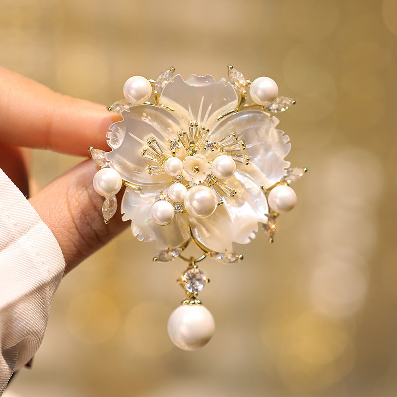 Decorative brooch with pearls and gold accents held by a hand against a blurred background