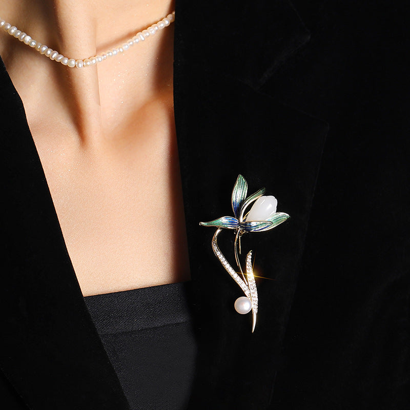 A close-up of a model wearing a black blazer, a pearl necklace, and a silver-toned enamel dragonfly brooch with green leaves and white pearls.