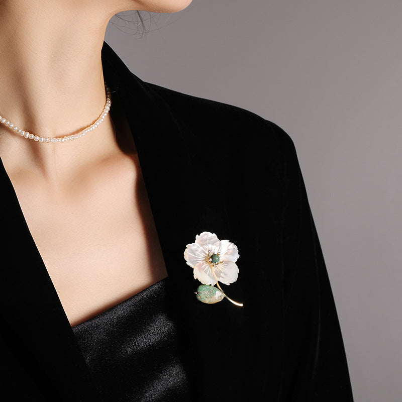 Woman wearing a black blazer with a white floral brooch and a gold necklace.