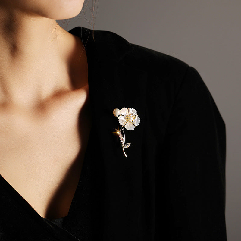A close-up of a person wearing a black velvet top and wearing a delicate flower brooch on the chest. The brooch features white enamel petals with gold-toned metal details and a small gold accent.