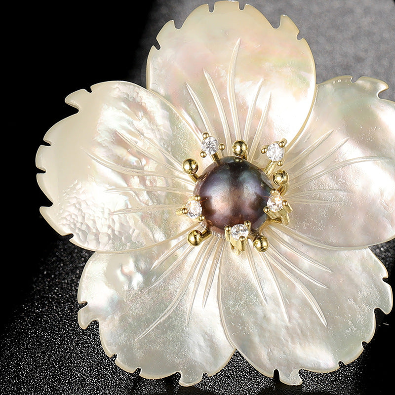 Floral brooch with pearl-like petals and central dark stone on a black background