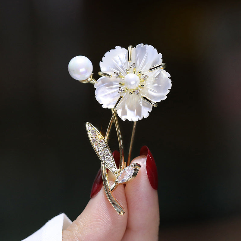 Floral brooch with pearls and crystals held by a hand against a dark background