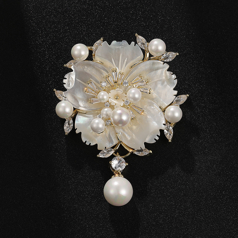 A floral pearl brooch featuring a large flower made of iridescent white mother-of-pearl petals, accented with small white pearls, clear rhinestones, and gold-tone metal details, set against a black background.