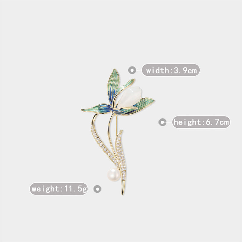 A gold-tone floral brooch with green and blue enamel leaves, a white pearl center, and a small pearl bead at the bottom, shown on a light gray background with measurement labels for width, height, and weight.