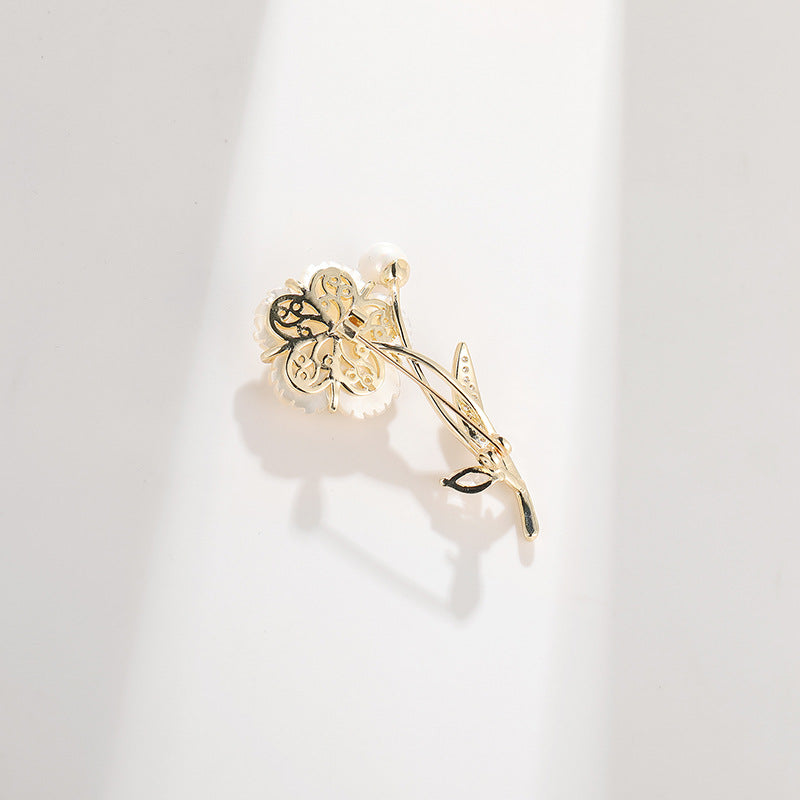 A delicate gold flower-shaped hair claw clip with a small white pearl accent, resting on a clean white surface with soft shadows.