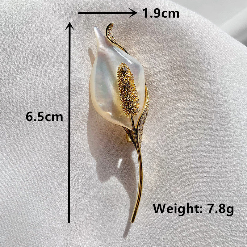 A calla lily flower-shaped brooch with a white iridescent pearl-like center, gold-toned leaf and spathe details, and small clear stones, shown on a light fabric background with measurement lines and text indicating 6.5 cm height, 1.9 cm width.