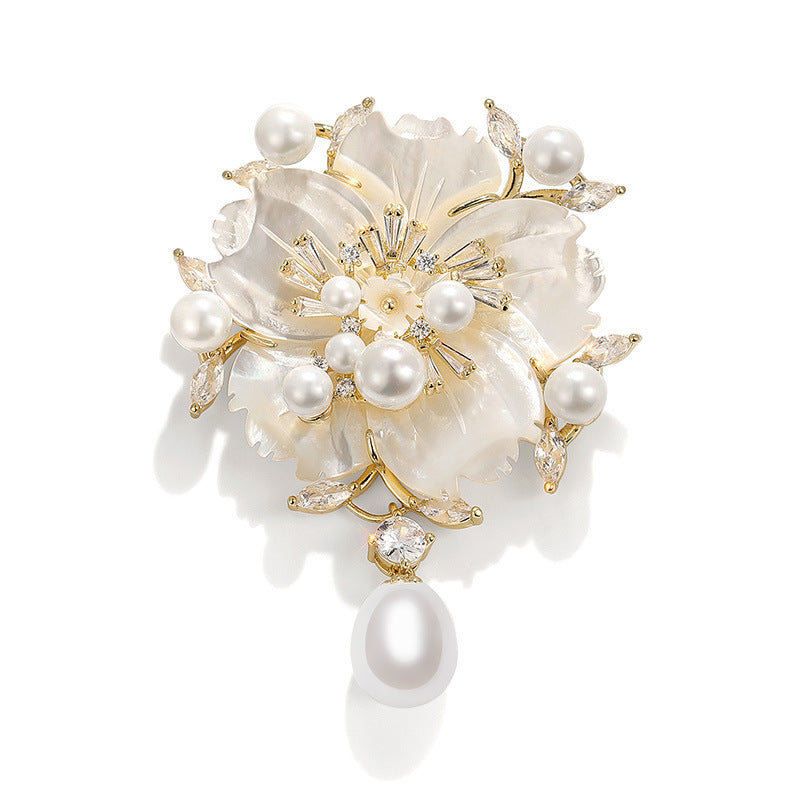 A floral brooch featuring white mother-of-pearl petals, freshwater pearls, and gold-tone metal accents with clear crystal details, shown on a white background.