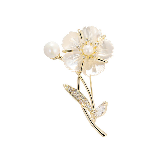 A gold flower brooch featuring a pearl flower with a gold center, a pearl bead on the stem, and a leaf adorned with small clear crystals, set against a clean white background.
