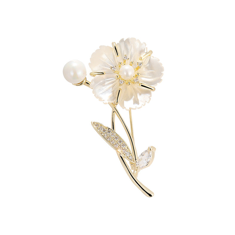 A gold flower brooch featuring a pearl flower with a gold center, a pearl bead on the stem, and a leaf adorned with small clear crystals, set against a clean white background.