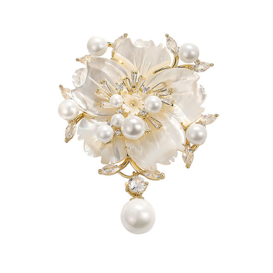 A gold and mother-of-pearl floral brooch featuring white pearls, clear rhinestones, and a dangling pearl drop, shown on a plain white background.