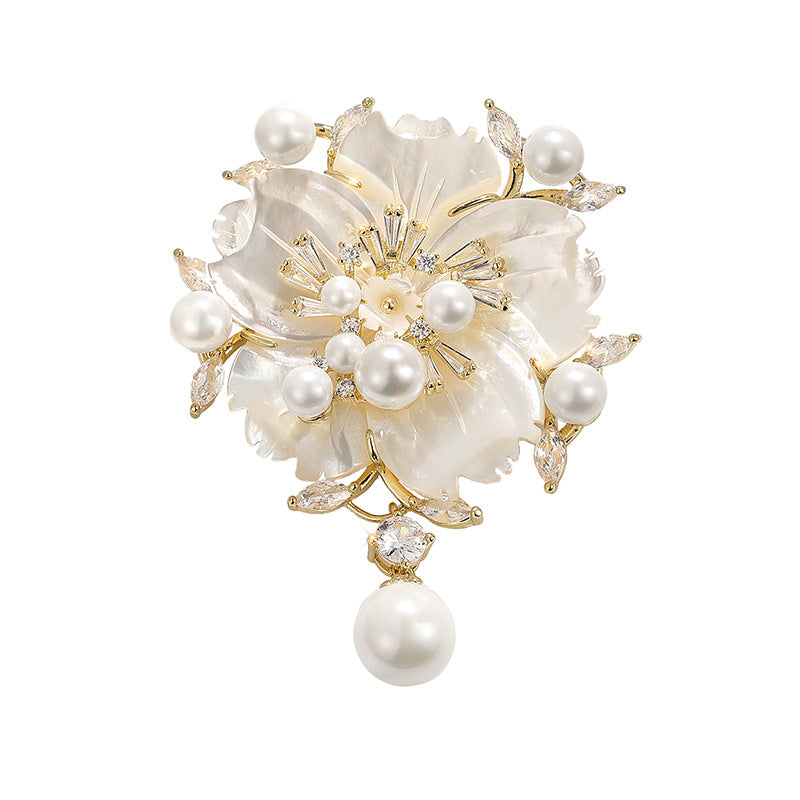 A gold and mother-of-pearl floral brooch featuring white pearls, clear rhinestones, and a dangling pearl drop, shown on a plain white background.